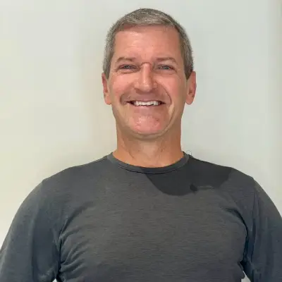 Smiling middle-aged man wearing a dark t-shirt against a plain background.