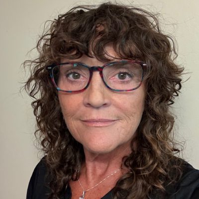 Portrait of a middle-aged woman with curly hair and glasses.